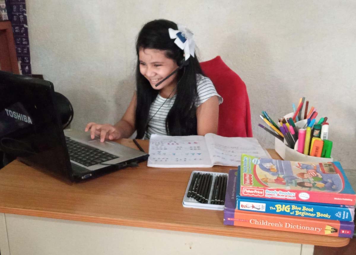 Younaly sitting at her wooden desk, smiling at her laptop while wearing headphones