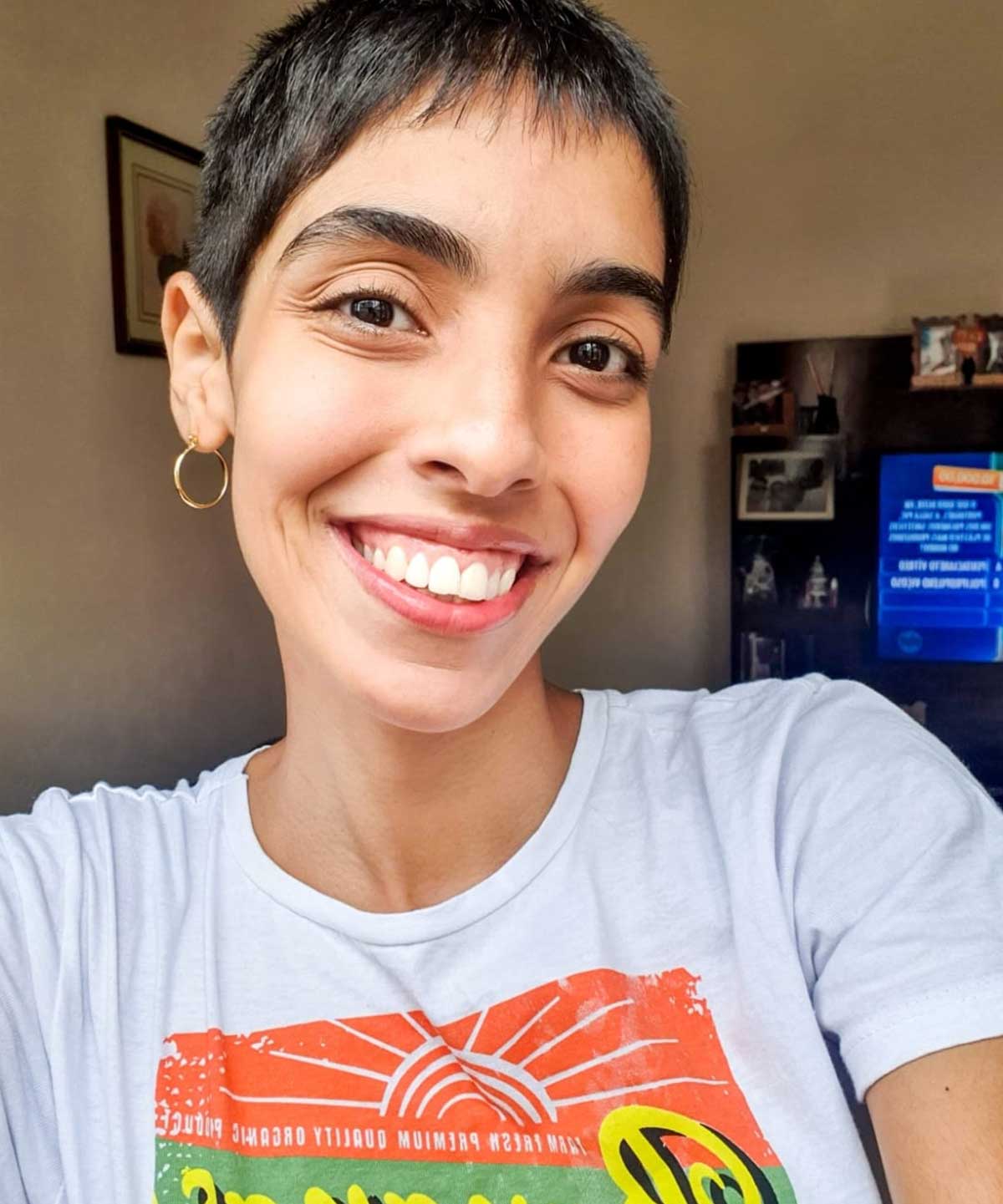 Smiling young woman with short brown hair, small hoop earrings, white t-shirt.