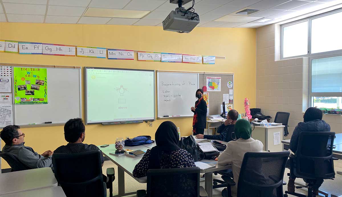 Madelyn standing at the front of a classroom speaking to six students sitting at their desk