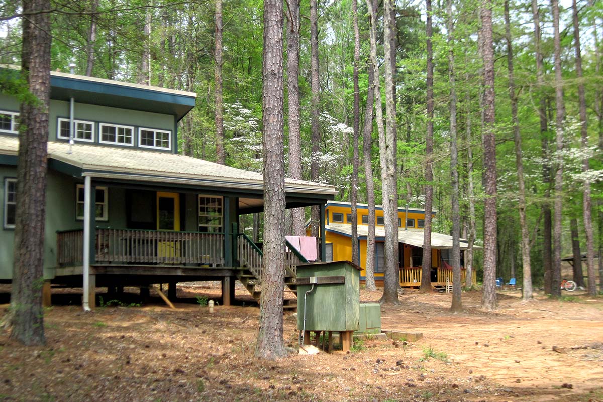 Two wooden houses with porches surrounded by trees.