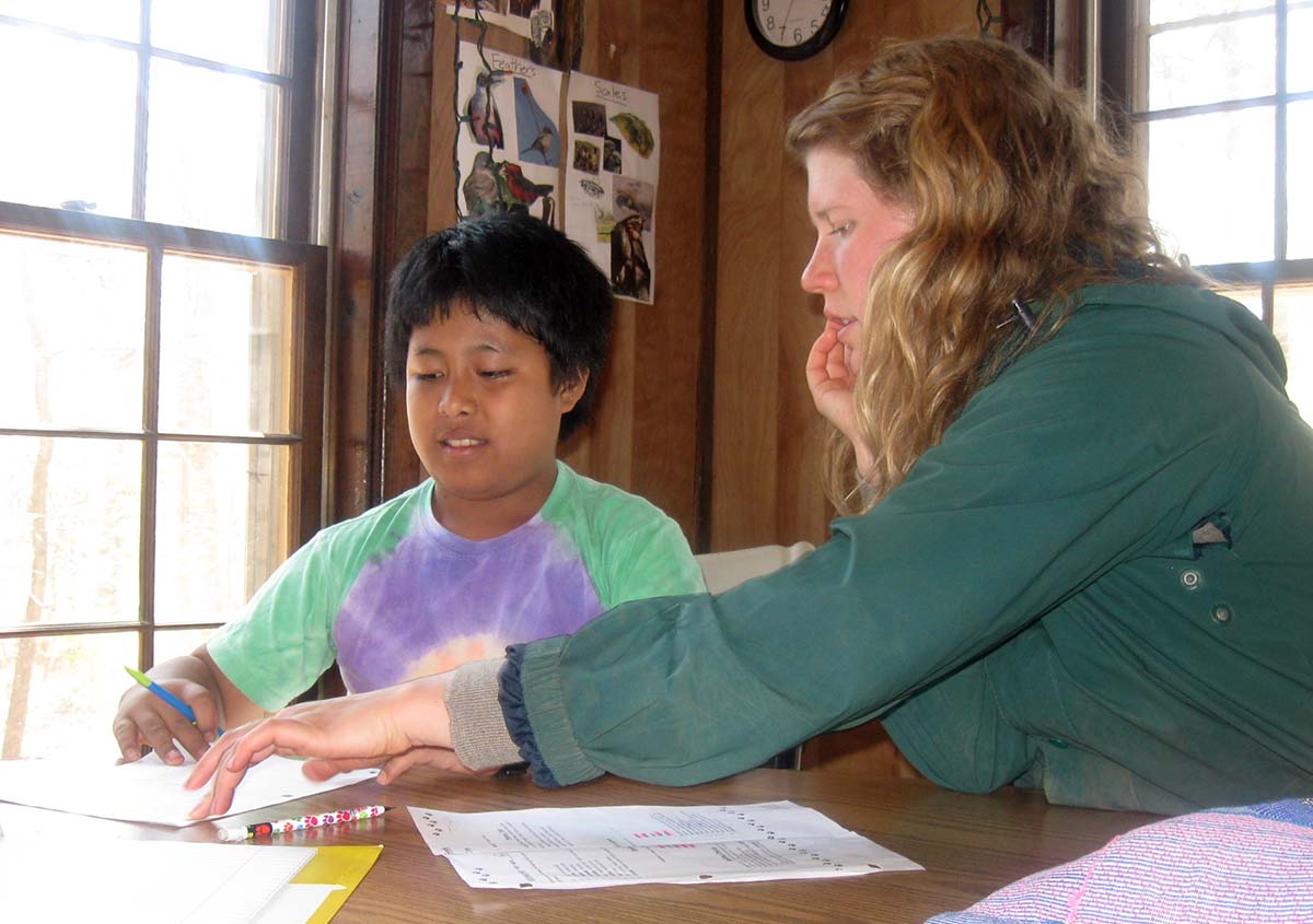 A girl is helping a young refugee student with their schoolwork.